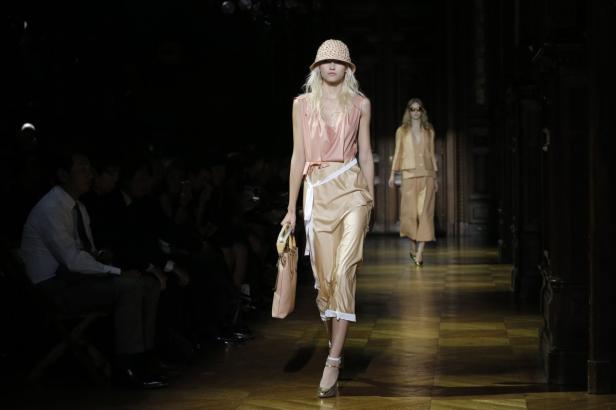 Eine blonde Frau in einem rosafarbenen Top und einem beigen Rock auf einem Laufsteg.