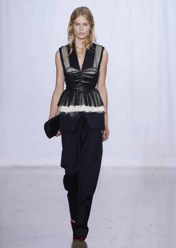 Eine Frau in einem schwarzen Oberteil und einer gestreiften Hose auf einem Laufsteg.