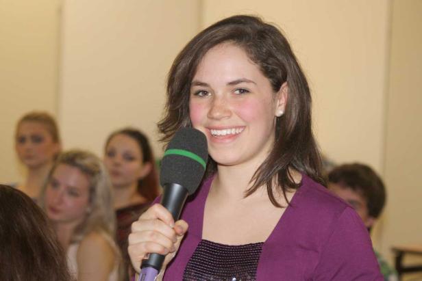 Eine junge Frau spricht in ein Mikrofon vor einem Publikum.