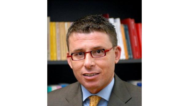 Ein Mann mit Brille und Anzug vor einem Bücherregal.