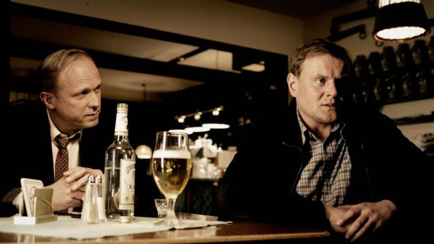 Zwei Männer sitzen an einem Tisch in einer Bar bei Bier und Schnaps.