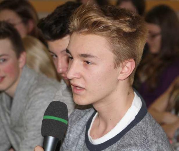 Ein junger Mann spricht in ein Mikrofon vor einer Gruppe von Menschen.