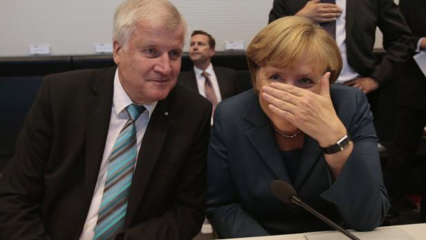 Angela Merkel hält sich die Hand vor das Gesicht, während Horst Seehofer daneben sitzt.