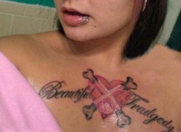 Eine Frau mit einem Lippenpiercing und einem Tattoo mit der Aufschrift „Beautiful Tragedy“ auf der Brust.
