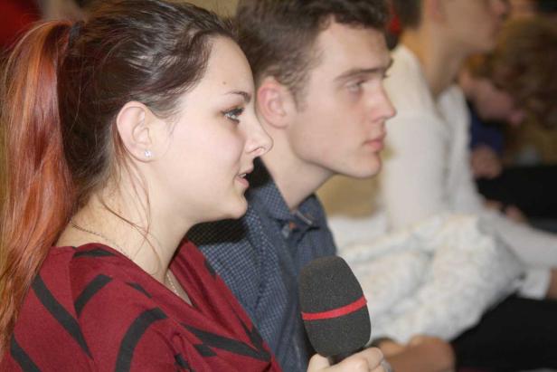 Eine junge Frau spricht in ein Mikrofon, neben ihr sitzt ein junger Mann.