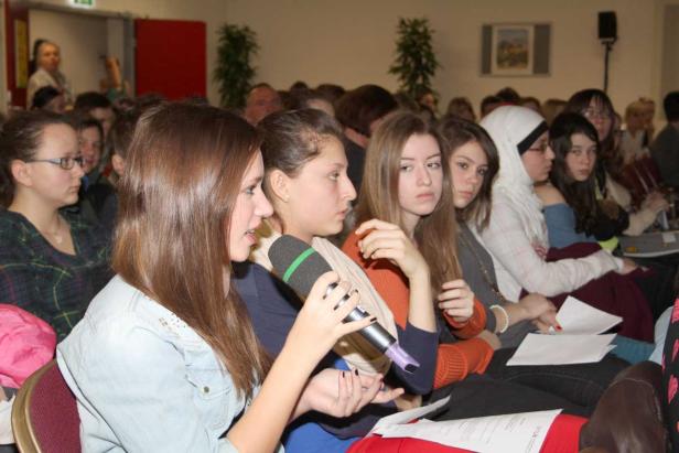 Eine junge Frau spricht bei einer Veranstaltung ins Mikrofon.