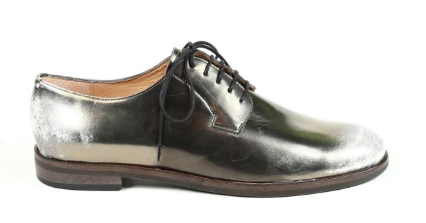 Ein silberfarbener Herrenschuh mit schwarzen Schnürsenkeln steht auf einem weißen Hintergrund.