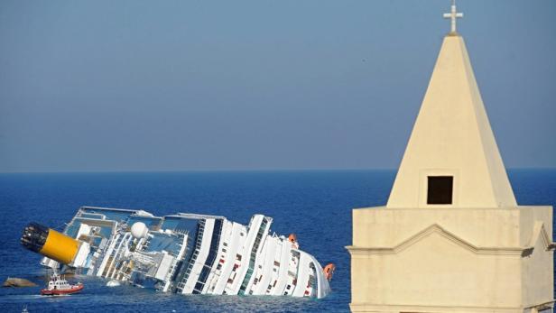 Die „Costa Concordia“ liegt gekentert im Meer, im Vordergrund ein Kirchturm.