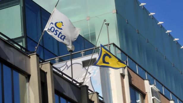 Zwei Flaggen mit dem Costa-Logo wehen vor einem modernen Gebäude.