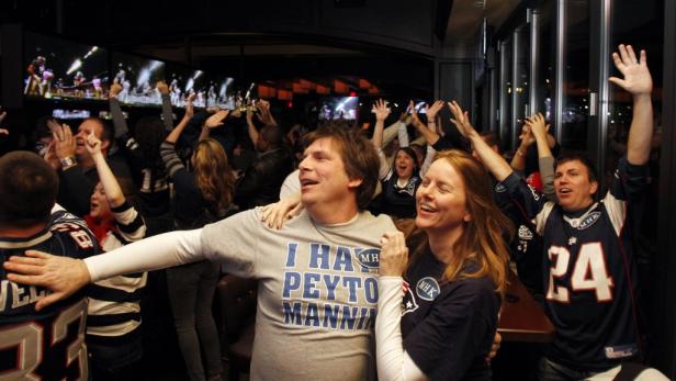 Eine Gruppe Football-Fans jubelt in einer Bar vor einem Fernsehbildschirm.