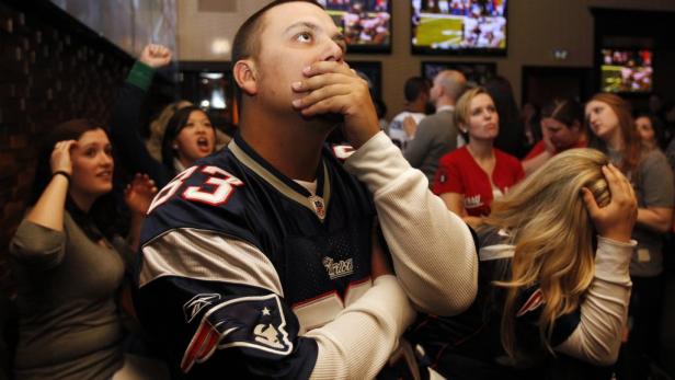 Eine Gruppe von Sportfans sieht besorgt auf einen der Fernseher in einer Bar.