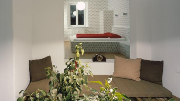 Ein Zimmer mit einem eingebauten Sitzbereich und einem Blick auf ein Schlafzimmer mit roter Bettwäsche.