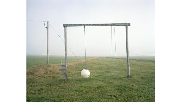 Eine Schaukel mit einem Ball als Sitz hängt in einer nebligen Landschaft.