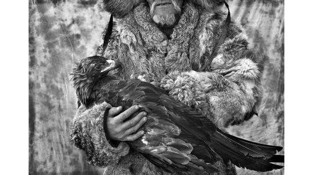 Ein Mann in Pelzkleidung hält einen Adler in seinen Händen.