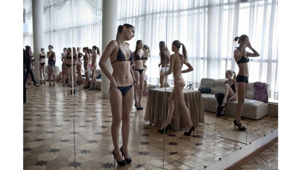 Eine Gruppe junger Frauen in Badebekleidung und High Heels steht in einem Raum mit Spiegeln.
