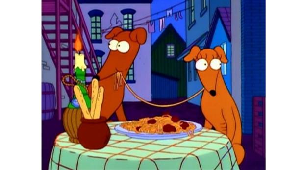 Zwei Hunde sitzen an einem Tisch mit Spaghetti und Brotstangen bei Kerzenlicht.