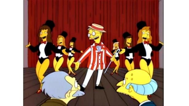 Eine Szene aus „Die Simpsons“ mit Tänzern und einem Mann im gestreiften Anzug auf einer Bühne.