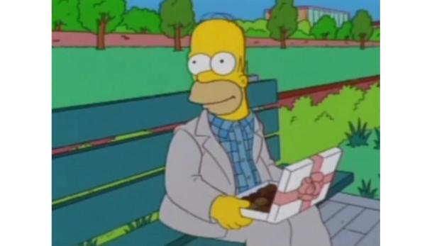 Homer Simpson sitzt auf einer Parkbank und hält eine Schachtel Pralinen.