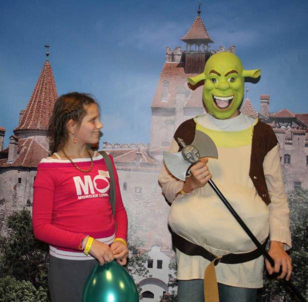 Ein Mädchen und eine als Shrek verkleidete Person posieren vor einem Schloss.