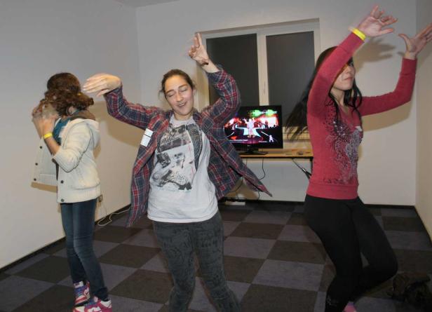 Drei junge Frauen tanzen vor einem Bildschirm, auf dem ein Tanzspiel läuft.