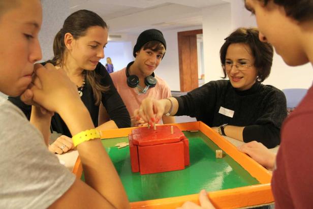 Eine Gruppe von Menschen spielt ein Geschicklichkeitsspiel mit einem roten Holzkasten.