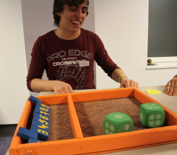 Ein junger Mann spielt ein Spiel mit Würfeln und Zahlen in einem orangefarbenen Rahmen.