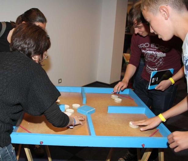 Mehrere Personen spielen ein Geschicklichkeitsspiel mit Holzscheiben auf einem blauen Tisch.