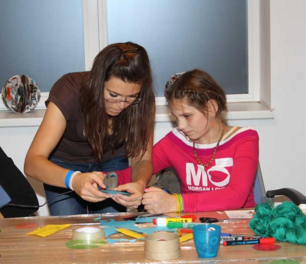 Eine Frau hilft einem Mädchen beim Basteln mit Papier und Schere.