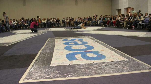 Eine Gruppe von Menschen sitzt um große Banner mit Unterschriften.