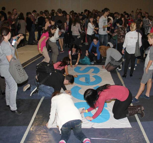 Eine Gruppe von Menschen unterschreibt ein großes Banner mit blauer Aufschrift.