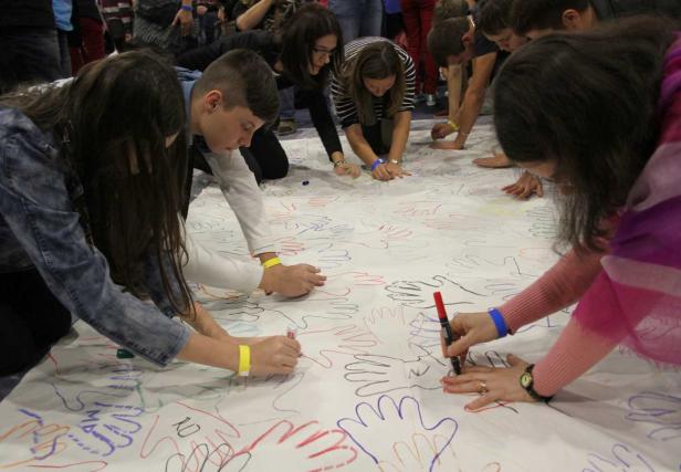 Eine Gruppe von Menschen zeichnet farbige Handumrisse auf ein großes Blatt Papier.