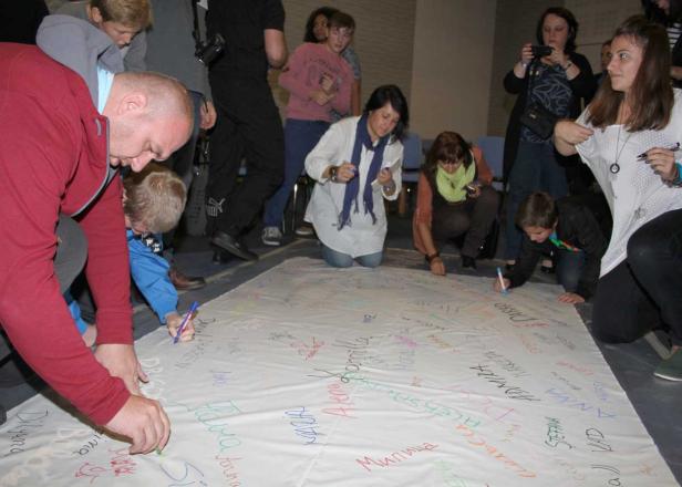 Mehrere Personen unterschreiben mit Stiften auf einem großen weißen Tuch.