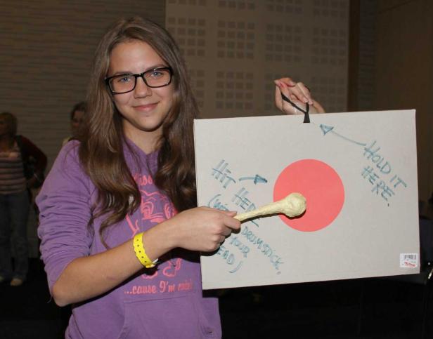 Ein junges Mädchen präsentiert ein selbstgemachtes Spiel mit einem Schläger und einer Zielscheibe.