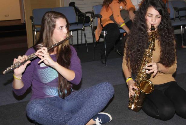 Zwei junge Frauen sitzen auf dem Boden und spielen Flöte und Saxophon.