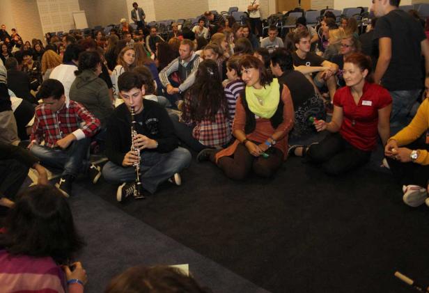 Eine Gruppe von Menschen sitzt auf dem Boden, ein junger Mann spielt Klarinette.