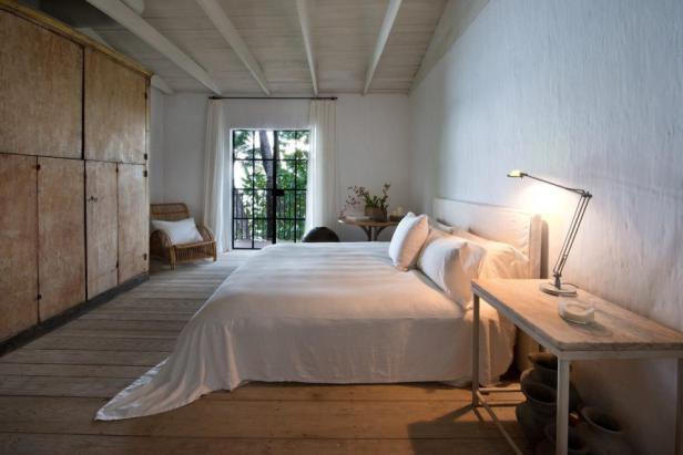 Ein helles Schlafzimmer mit Holzboden, großem Bett und Blick ins Grüne.