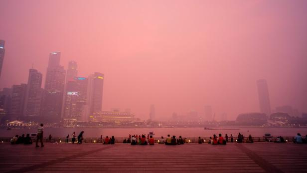 Menschen sitzen am Ufer von Singapur im Dunst.