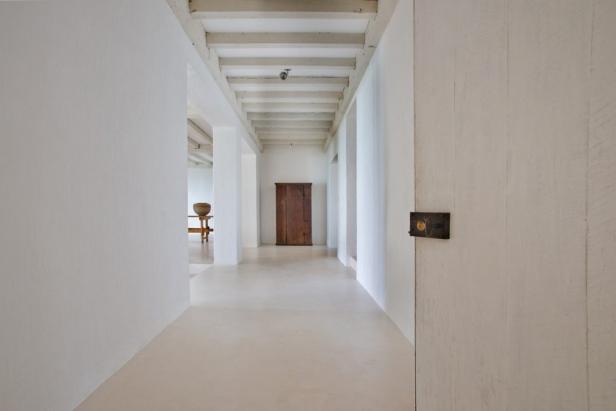 Ein langer, weißer Flur mit Holzbalkendecke und einem alten Schrank am Ende.