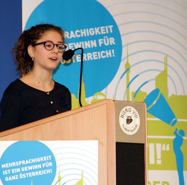 Eine junge Frau mit Brille spricht an einem Rednerpult mit dem Logo BGRG VIII Albertgasse.