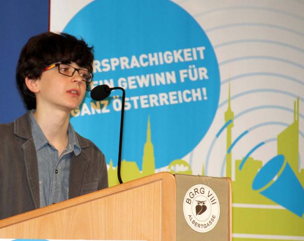 Ein junger Mann mit Brille hält eine Rede an einem Rednerpult.