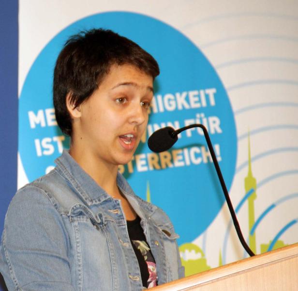 Eine junge Frau spricht bei einer Veranstaltung am Rednerpult.