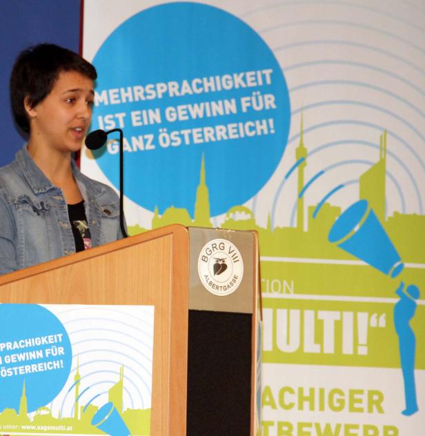Eine junge Frau spricht auf einer Veranstaltung vor einem Banner zum Thema Mehrsprachigkeit.
