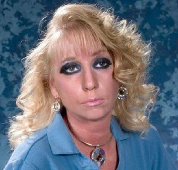 Eine Frau mit blonden, gelockten Haaren und starkem, dunklem Augen-Make-up blickt in die Kamera.