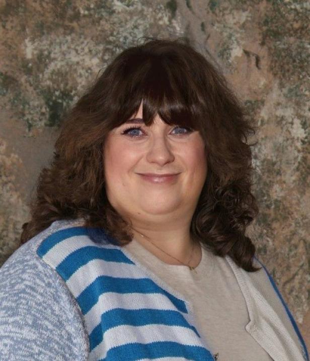 Eine Frau mit braunen Haaren und blau gestreifter Strickjacke lächelt in die Kamera.