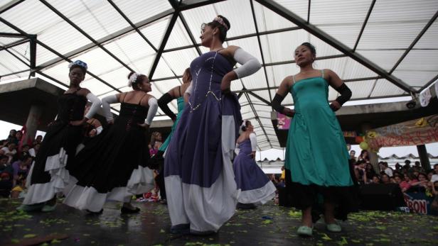 Eine Gruppe von Frauen in farbenfrohen, traditionellen Kleidern tanzt auf einer Bühne vor Publikum.