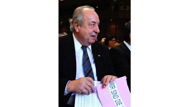 Ein Mann im Anzug hält ein rosa Papier mit der Aufschrift „Wir sind die T…“.