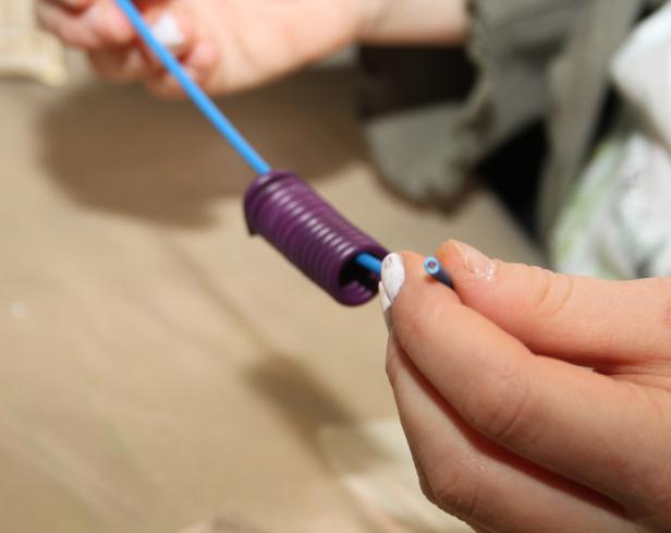 Eine Person fädelt einen blauen Draht in eine lila Spirale ein.