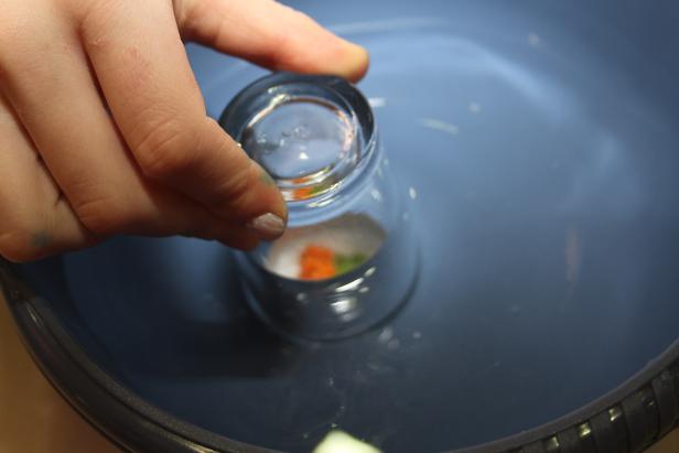 Eine Hand hält ein Glas über eine Schüssel mit Wasser und Gemüse.