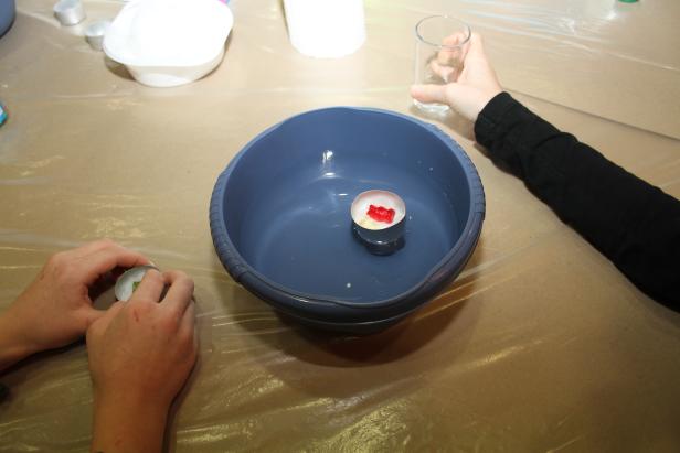 Menschen basteln schwimmende Teelichter mit Gummibärchen in einer Wasserschale.
