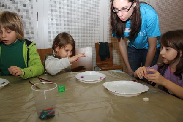 Kinder experimentieren mit Farben und Wasser unter Aufsicht einer Betreuerin.